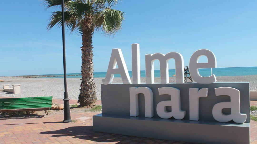 Cartell d'Almenara a la platja amb una palmera